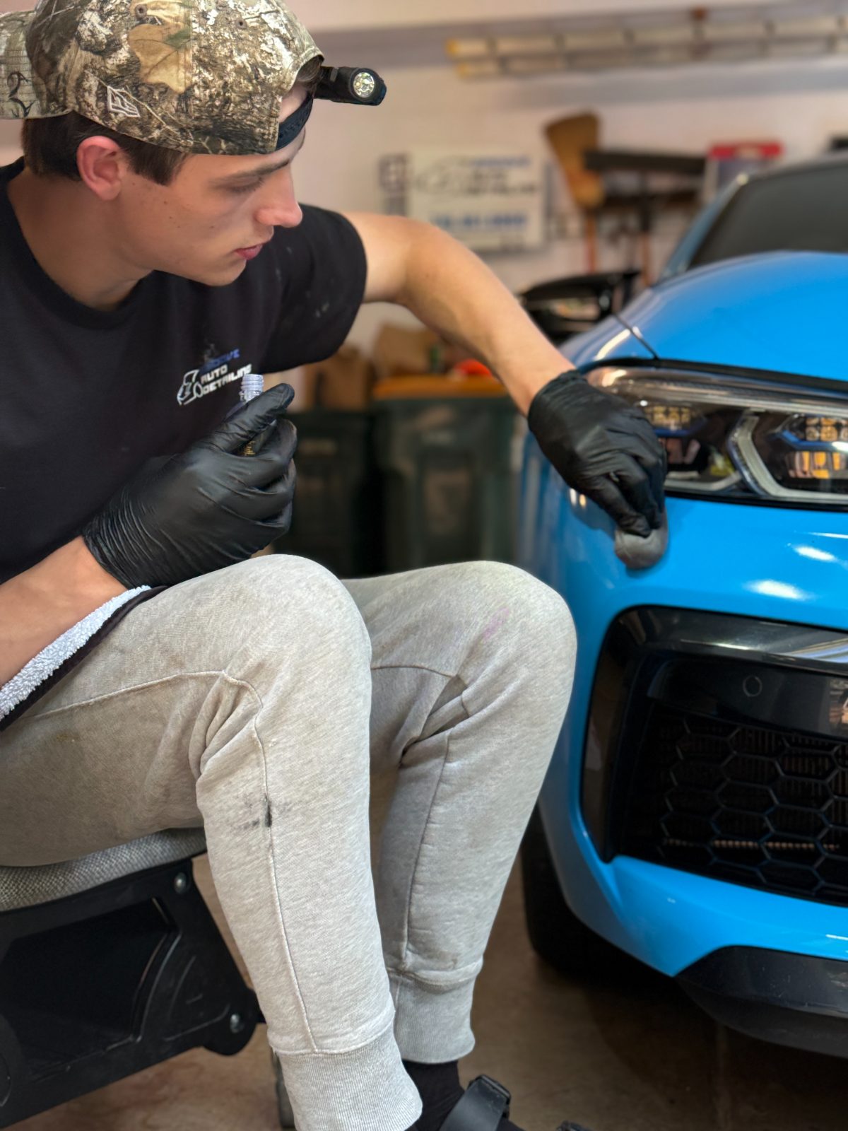 Smoove detailer with a headlamp inspecting the front end of a blue BMW M8 — detail-obsessed team Eau Claire