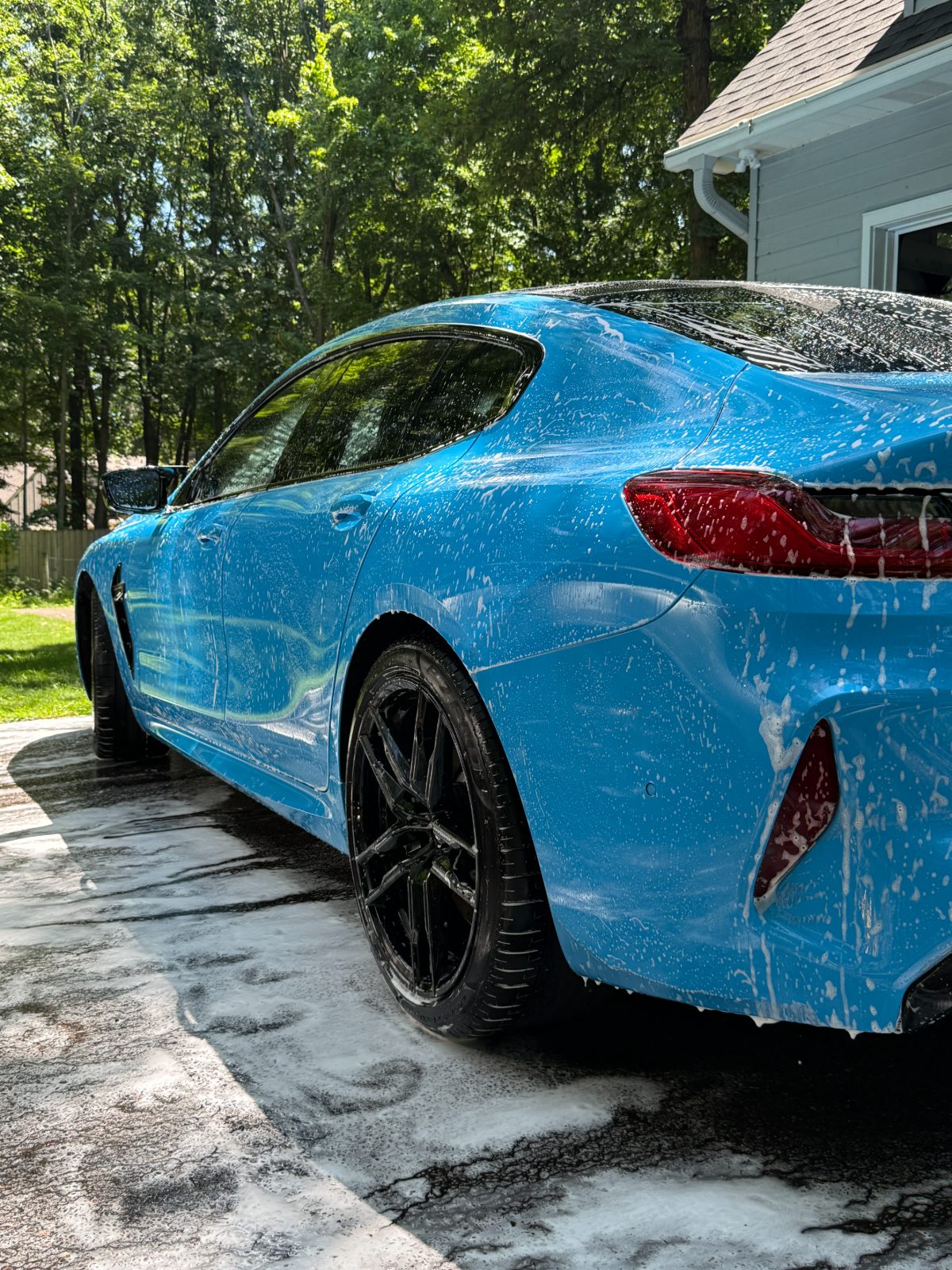 Blue BMW M8 covered in thick foam during a mobile detail in an Eau Claire driveway