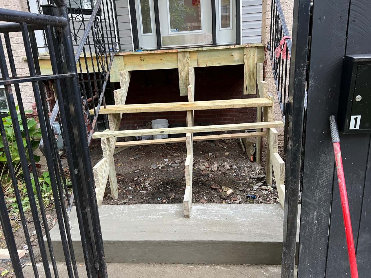 Outdoor wood framing beside a black iron fence with a ladder leaning nearby