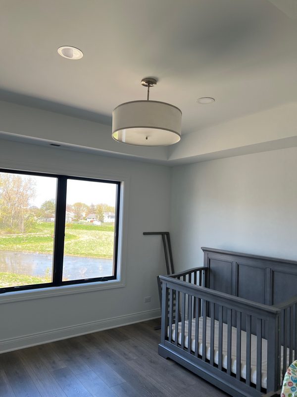 Bedroom with a gray wood-look floor, a crib and a large black-framed window