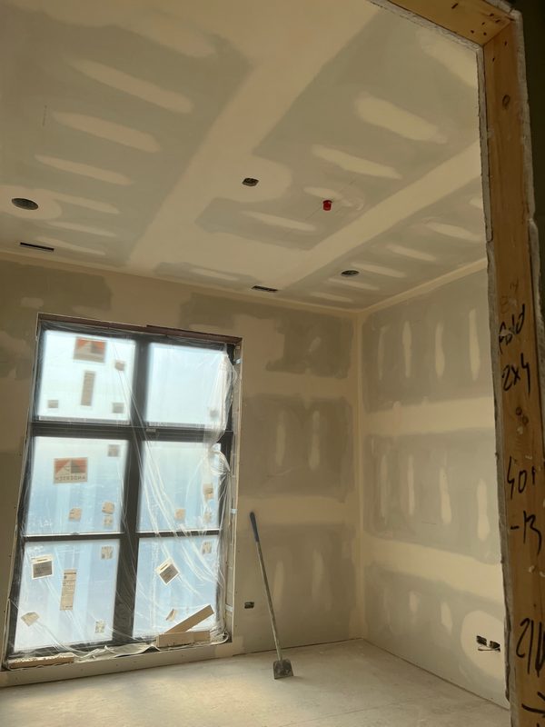 Room with taped drywall and a plastic-covered window during renovation