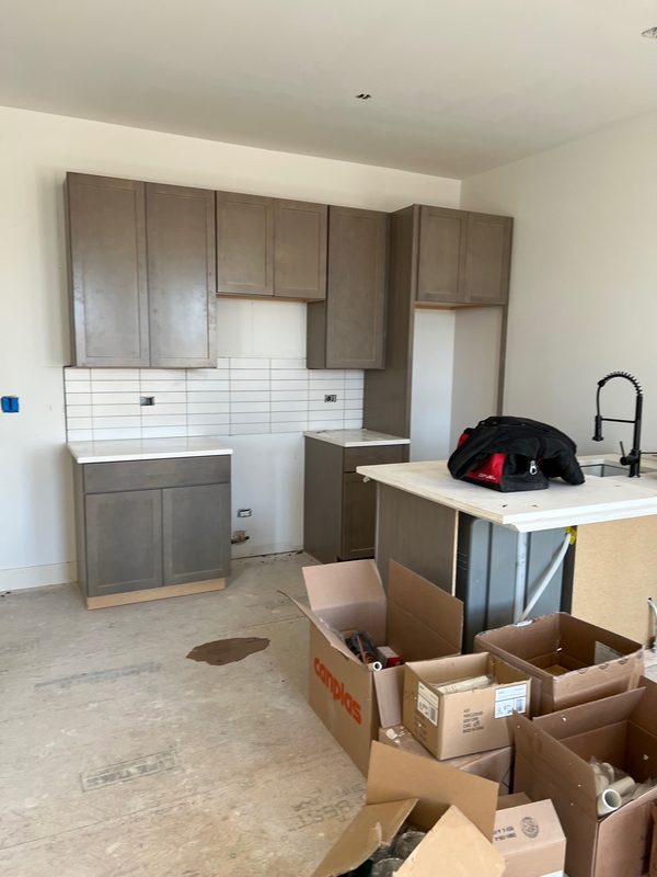 Kitchen under renovation with gray cabinets, a white tile backsplash and an island with a white countertop