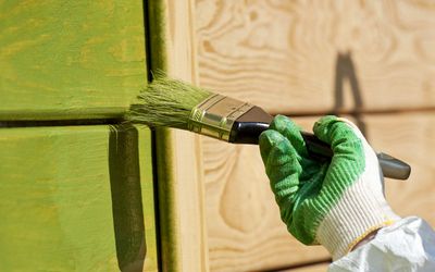 Brush applying green paint over a textured wall