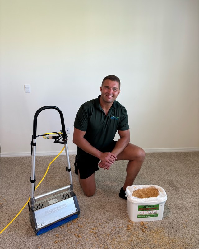A Swift Dry technician kneeling beside the brush machine and a tub of dry cleaning compound