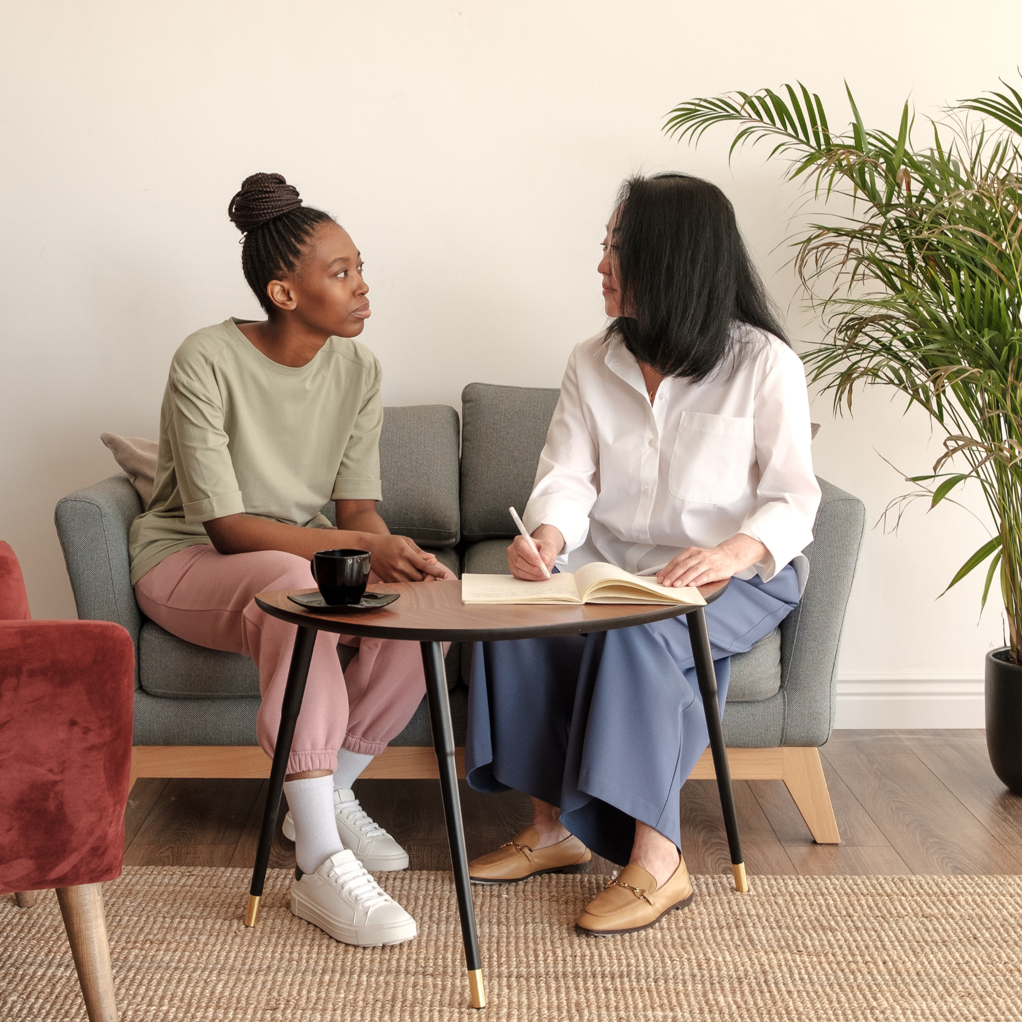 Two women having a coaching session on a couch, one taking notes, supportive conversation