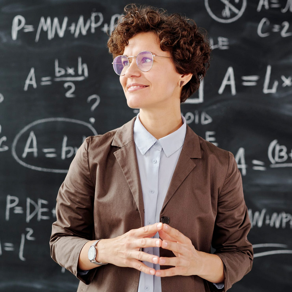 A teacher smiling in front of a chalkboard covered in handwritten equations