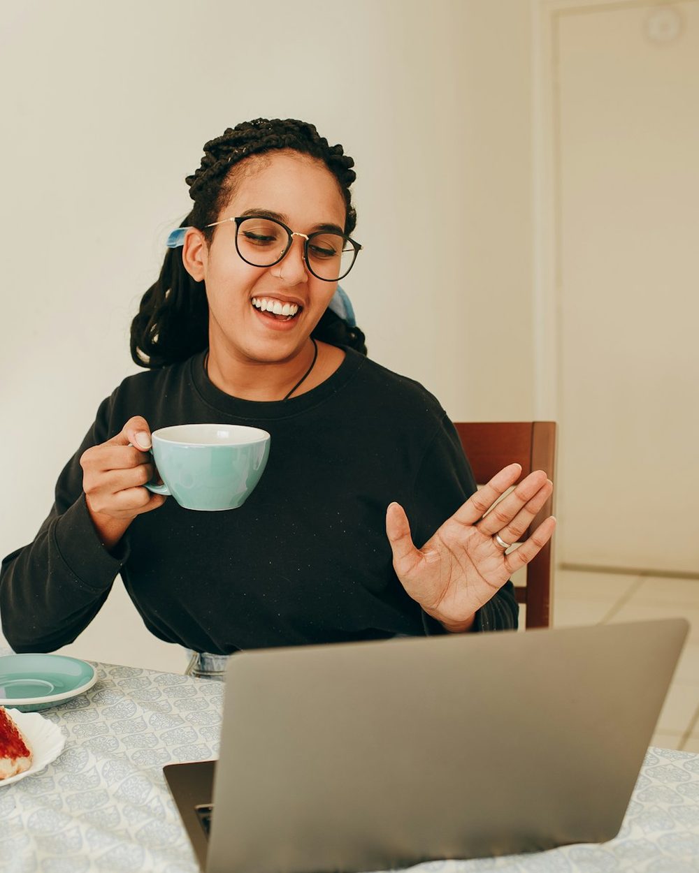 A woman smiling and holding a cup of tea while talking on a video call on her laptop