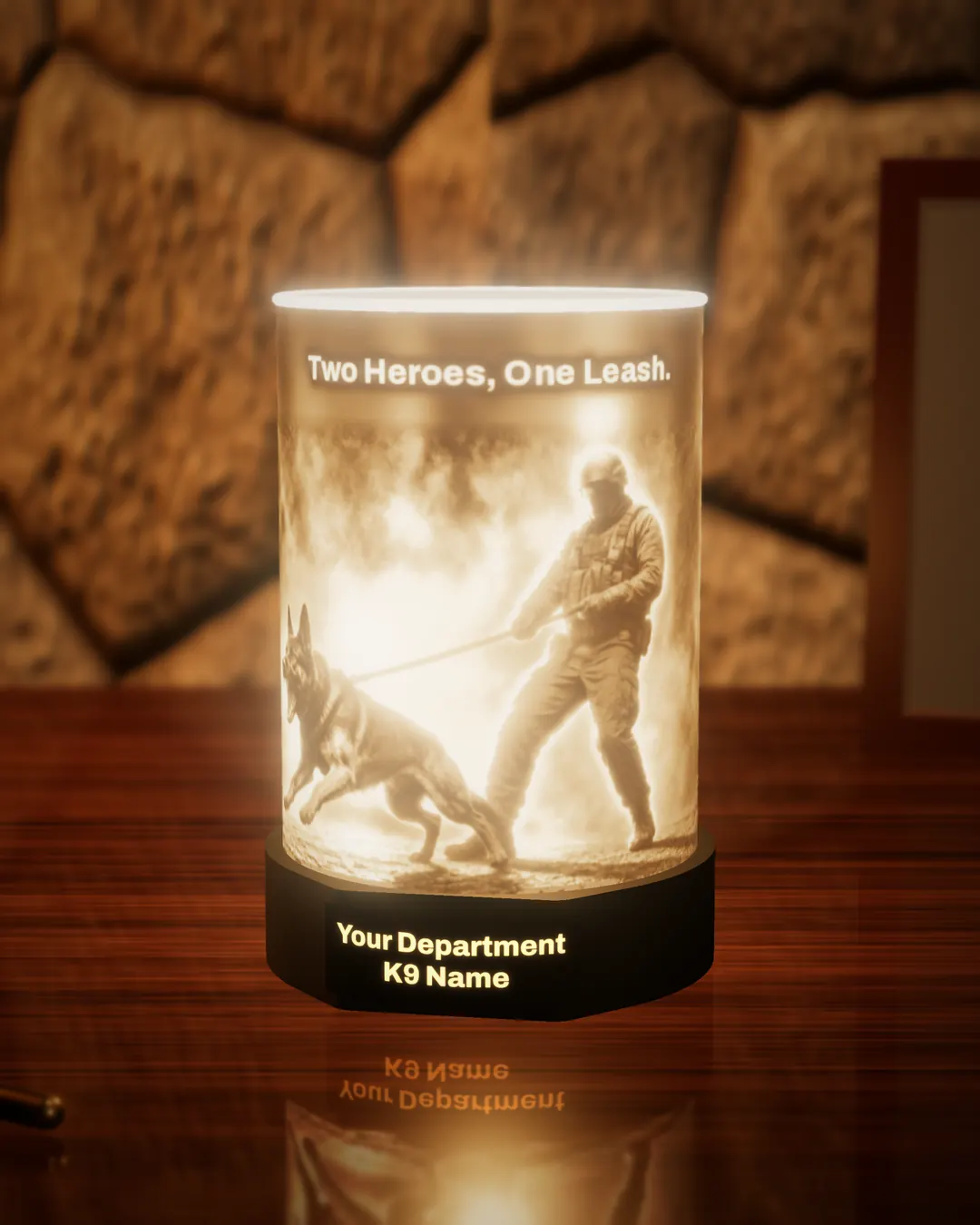 K9 handler tribute lithophane lamp lit warm, showing a police dog lunging on a tight leash beside its handler, under the glowing words “Two Heroes, One Leash.”, with the black base nameplate glowing “Your Department / K9 Name”, on a wooden desk against a stone wall