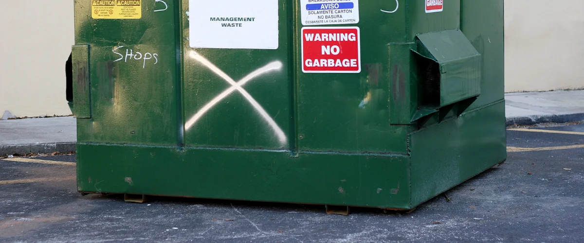 A large green dumpster with a white painted 'X' and a "Warning No Garbage" sign on its side. A large green dumpster with a white painted 'X' and a "Warning No Garbage" sign on its side.