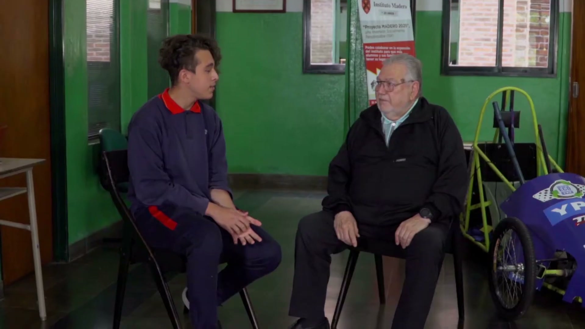 Un tutor charlando con un alumno, con el auto del Desafío ECO al costado