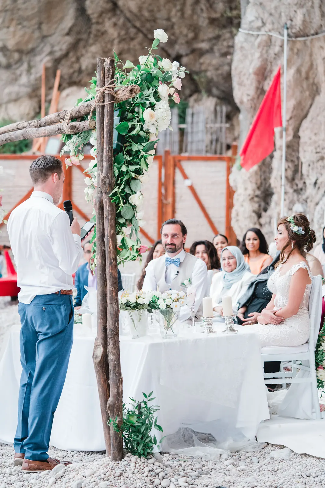 An outdoor wedding ceremony in Sicily on a terrace above the sea, with a simple floral frame and guests seated close