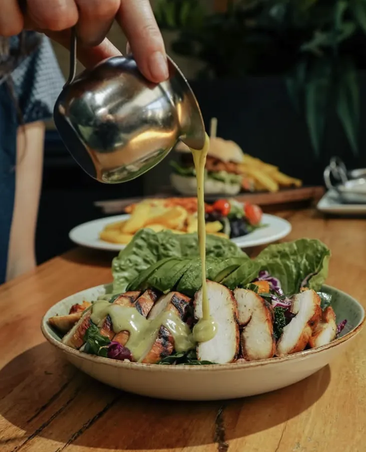 Grilled chicken and avocado salad with dressing being poured