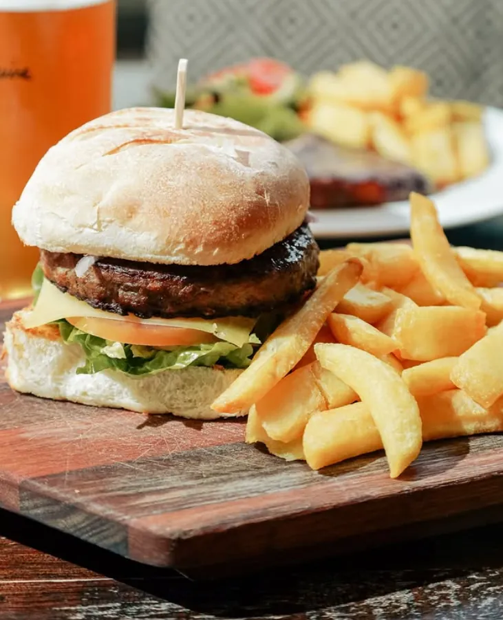 The Cally burger with potato wedges on a timber board and a beer
