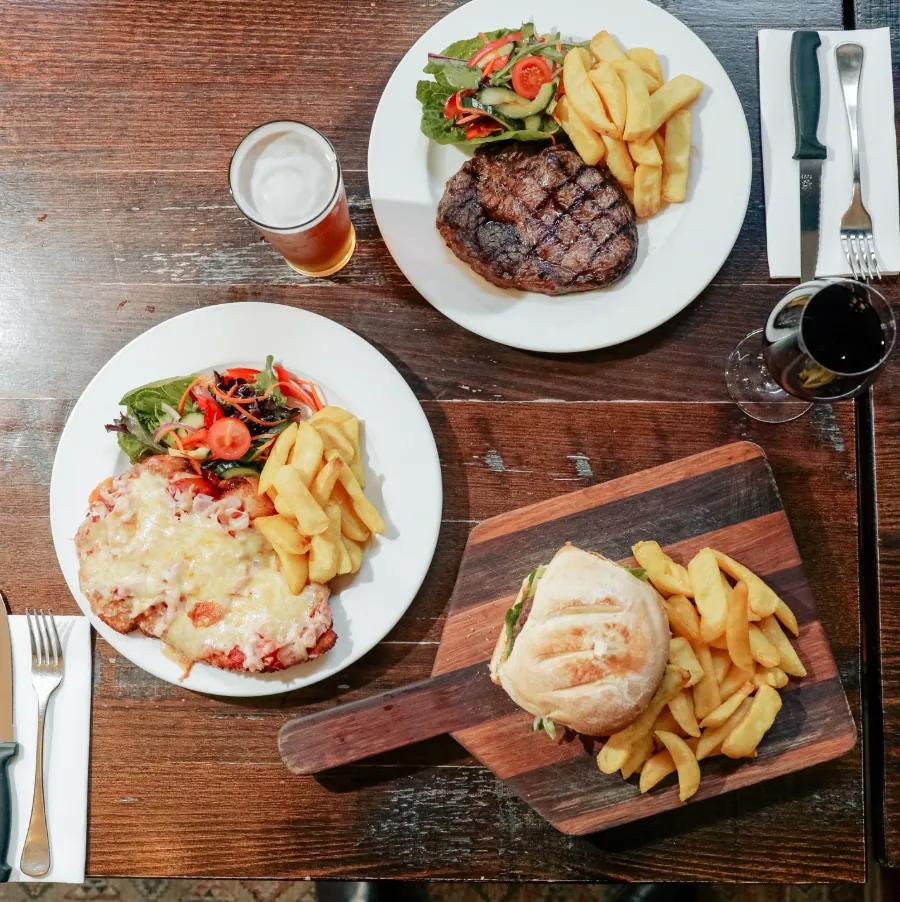 Steak, parma and burger plates with potato wedges on a pub table