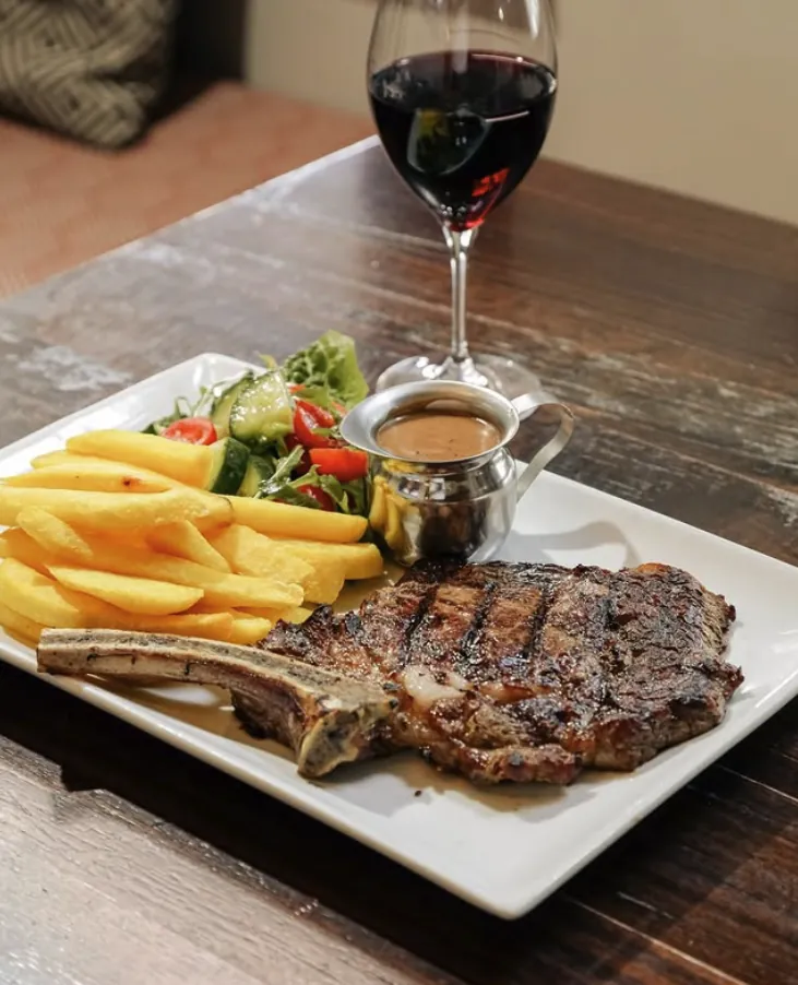 Rib-eye on the bone with potato wedges, salad and a glass of red wine