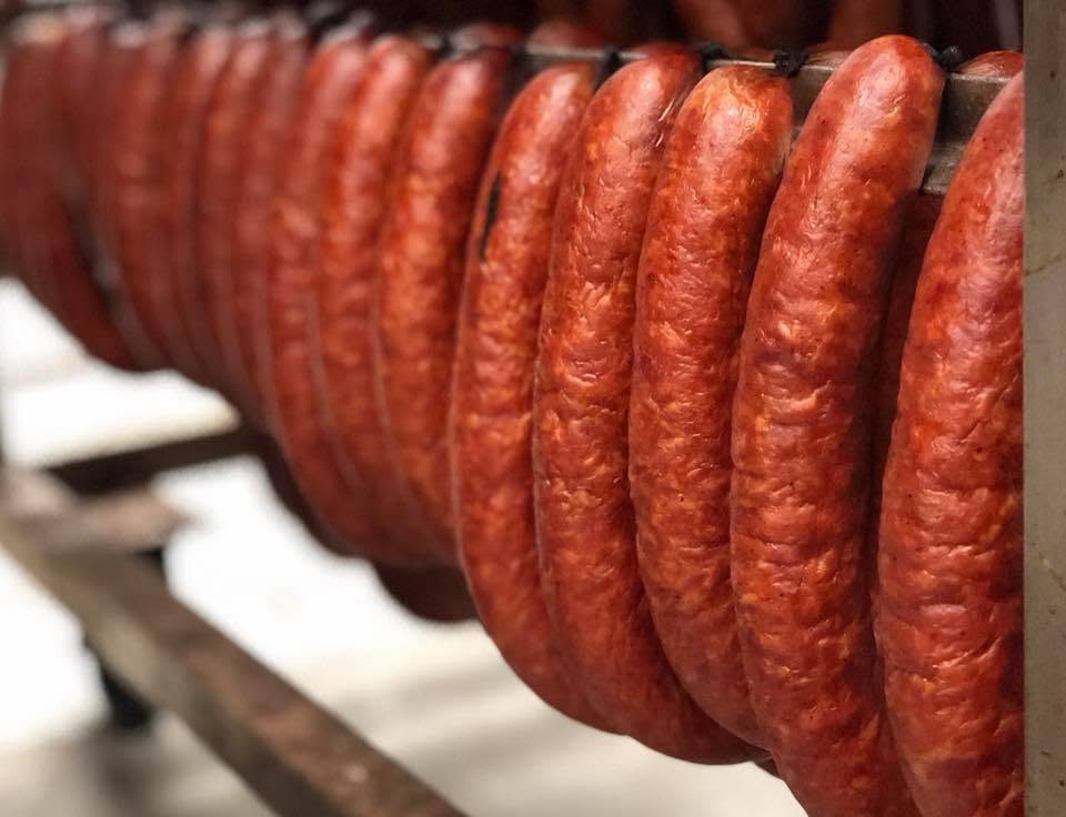 Rings of house-made smoked sausage hanging in the smokehouse