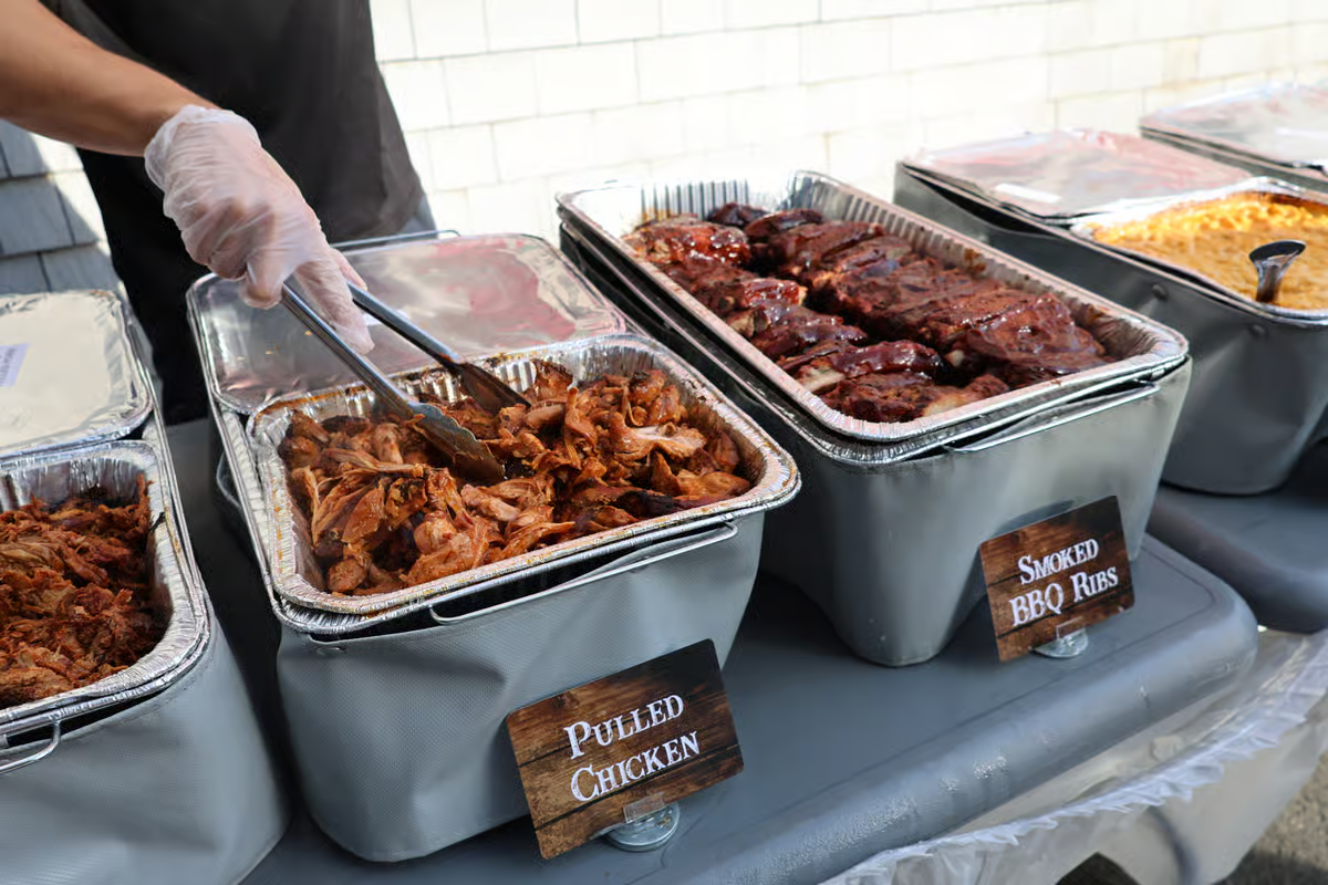 A Jordan Meats catering line with pans of pulled chicken, smoked BBQ ribs and pulled pork