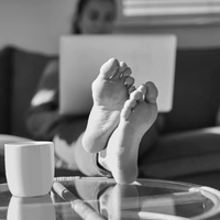 A person on a couch using a laptop with their feet up on the coffee table.