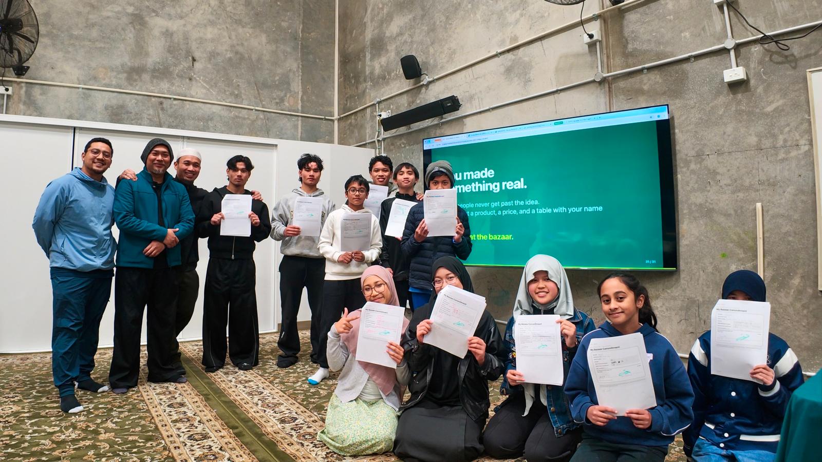 Young makers and mentors holding up their signed bazaar commitments at the KUM Centre