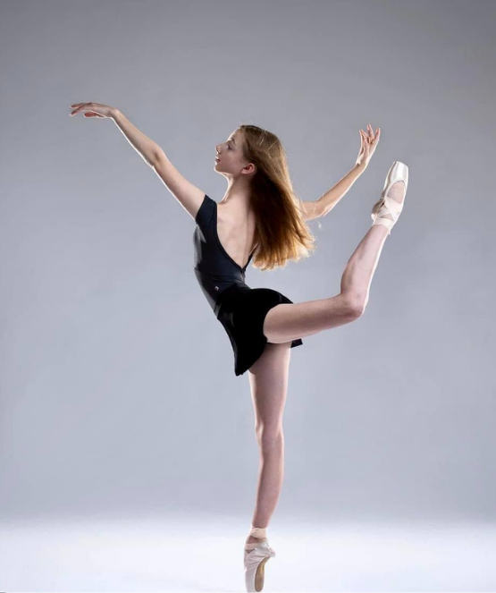 A joyful young dancer reaching upward in a sunlit studio