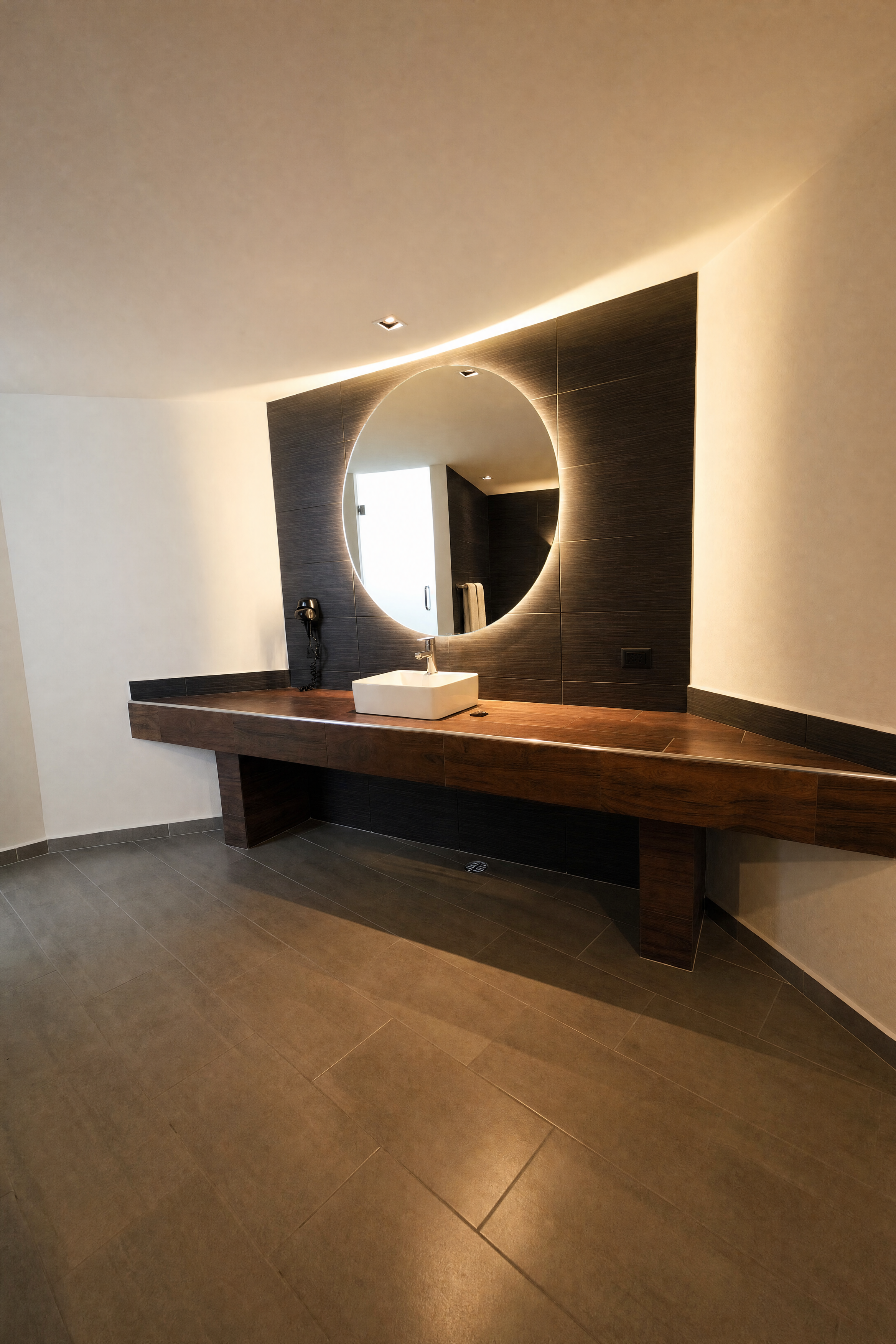 Área de lavabo de Motel Speed con espejo circular iluminado y cubierta de madera