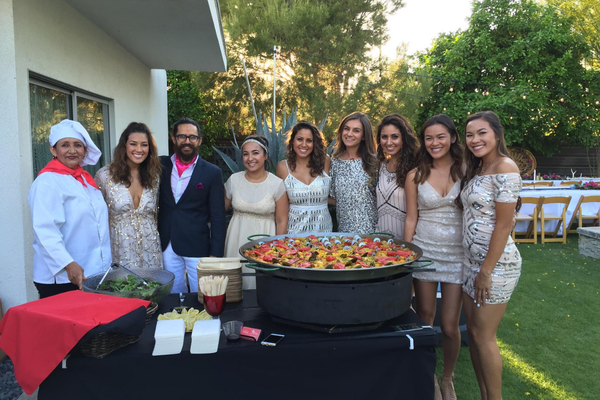 Guests gathered around a paella station with the chef at a backyard celebration