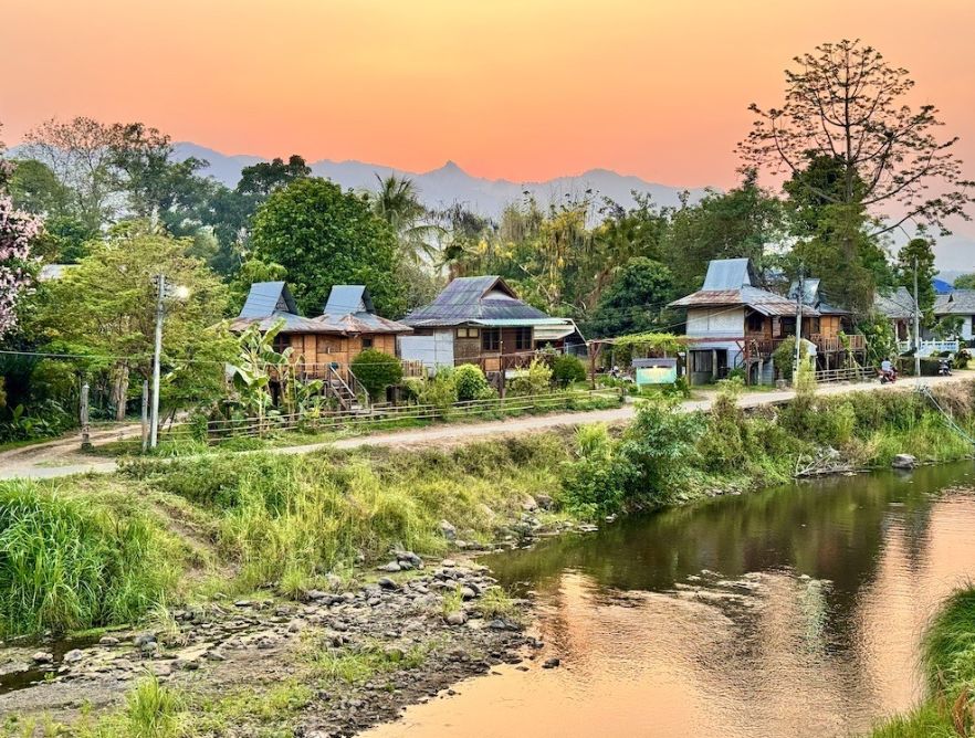 Wooden houses by the Pai River under a pink and orange sunset sky