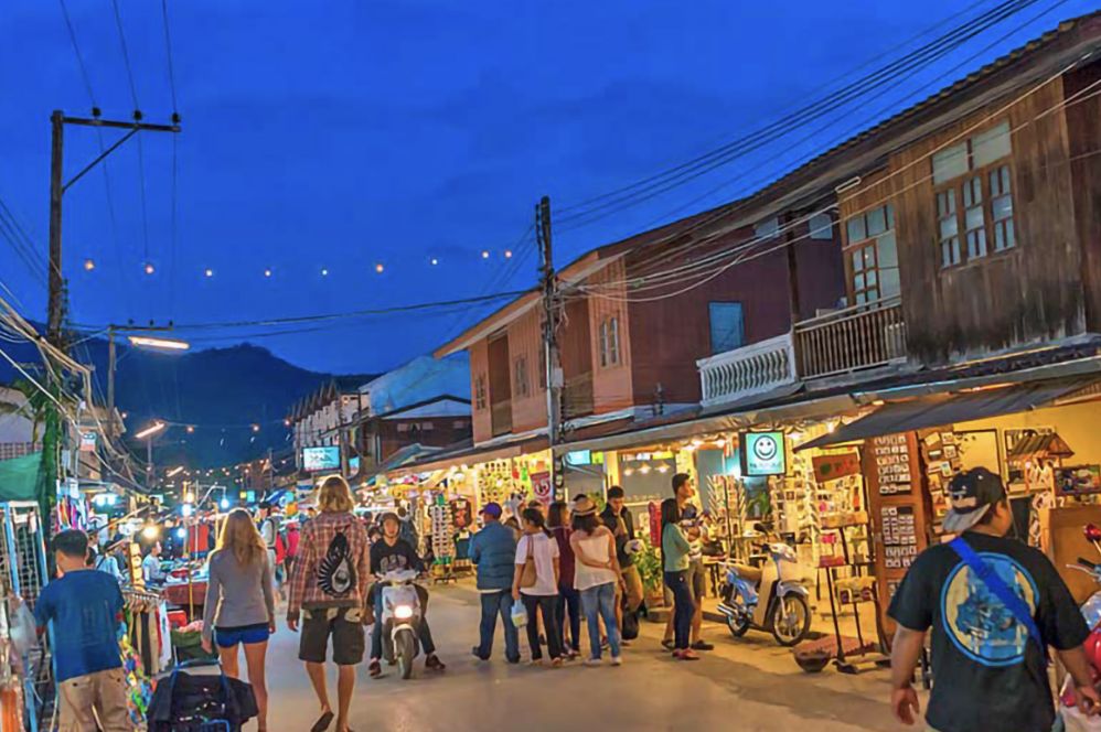 Travelers strolling Pai Walking Street at dusk under string lights