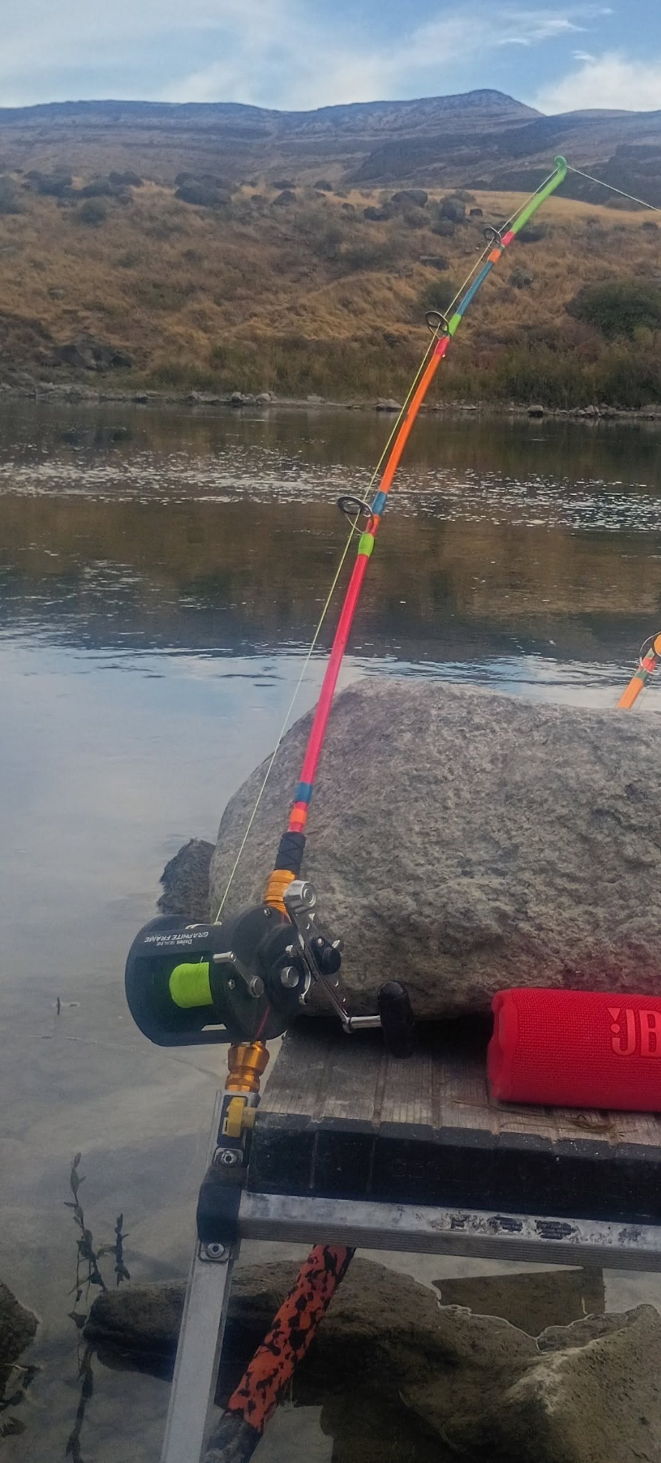 A brightly colored Compensator rod and reel beside a river