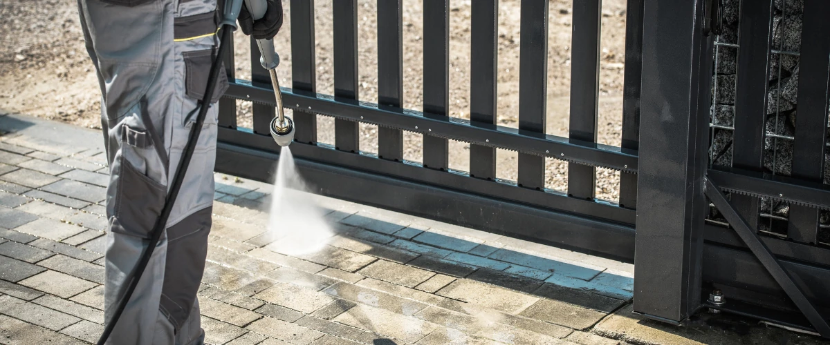Worker using a pressure washer to clean a brick driveway near a metal gate. Worker using a pressure washer to clean a brick driveway near a metal gate.