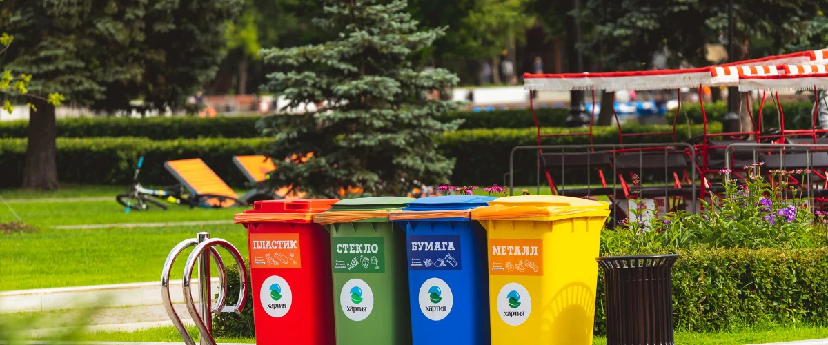 Four brightly colored recycling bins for plastic, glass, paper, and metal in a green park environment. Four brightly colored recycling bins for plastic, glass, paper, and metal in a green park environment.