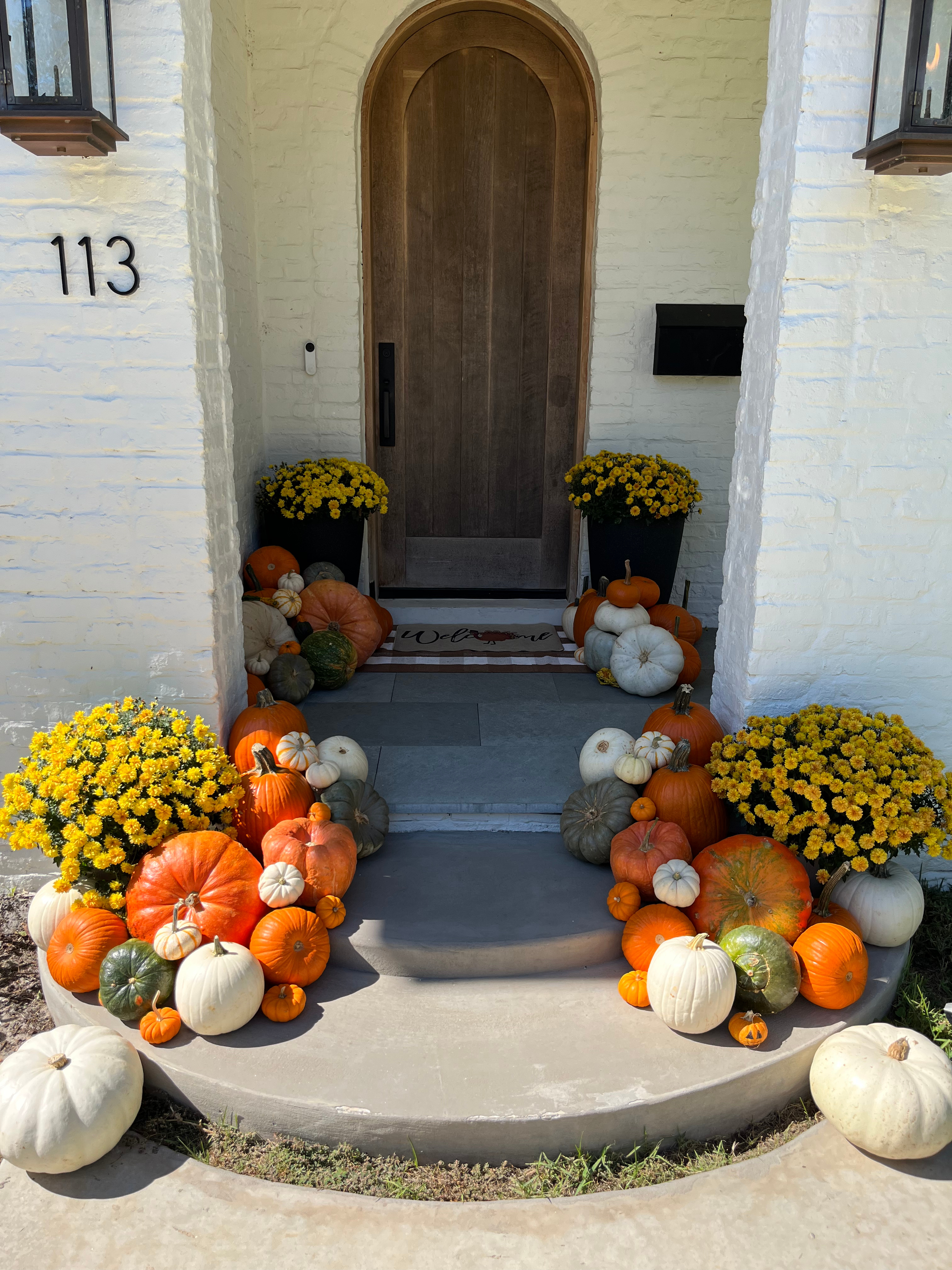 A front porch styled with pumpkins, gourds, and hay bales