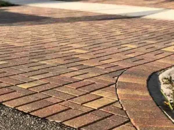 Close-up view of a herringbone patterned paver driveway in shades of brown and red, with a curved edge.