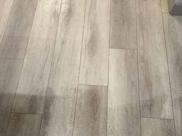 Close-up of light-colored wood laminate flooring with distinct grain patterns and varied plank lengths.