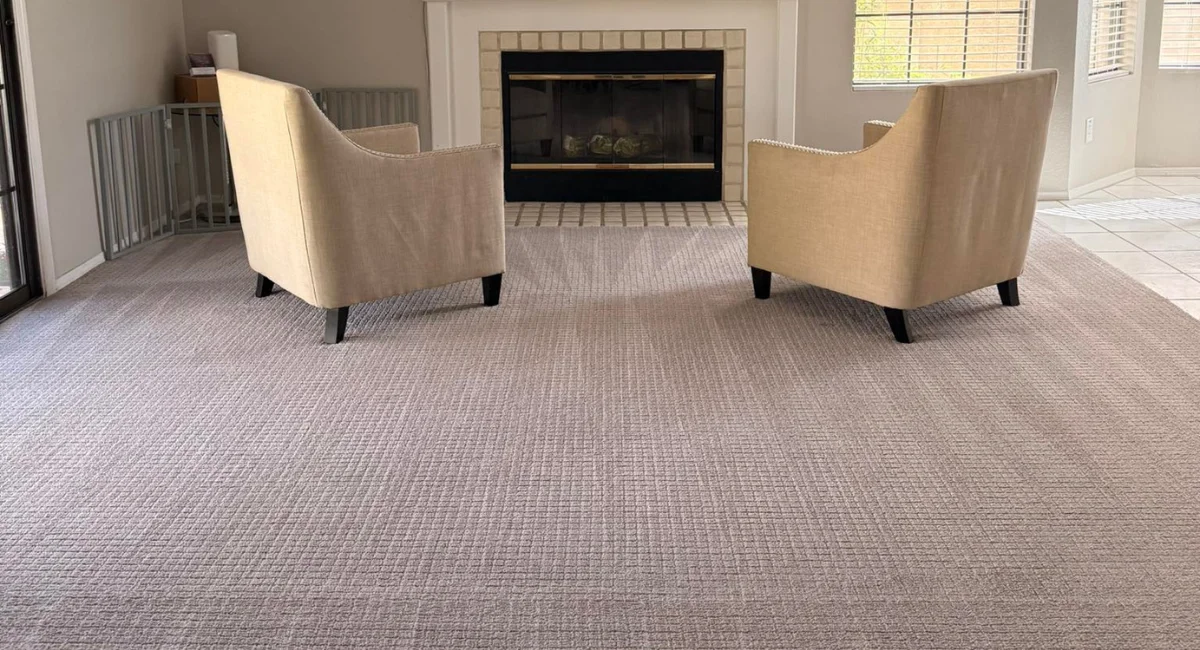 A wide shot of a living room with light gray patterned wall-to-wall carpeting and two beige armchairs facing a fireplace. A wide shot of a living room with light gray patterned wall-to-wall carpeting and two beige armchairs facing a fireplace.
