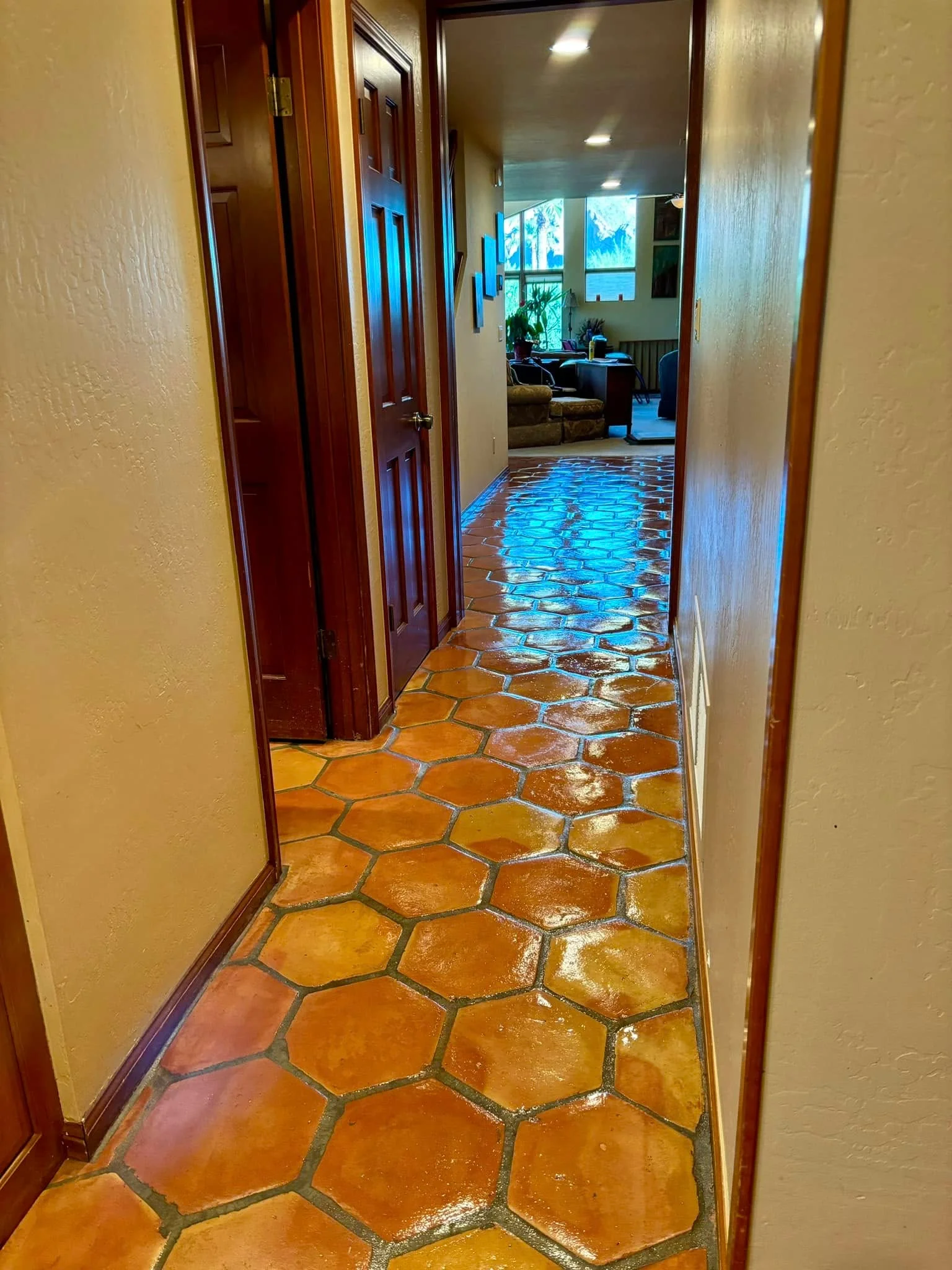 A long hallway with shining hexagonal terra cotta floor tiles and light beige walls leading to a brighter room.