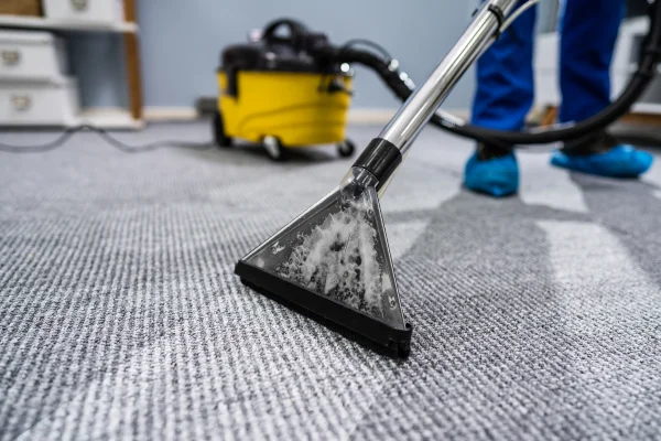A carpet cleaning machine extracting dirt from a gray carpet, with a vacuum unit in the background.