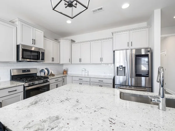 A clean, bright modern kitchen with white cabinets, stainless steel appliances, and a granite countertop island.