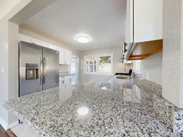 A modern kitchen showcasing speckled granite countertops, white cabinets, and stainless steel appliances with bright window light.