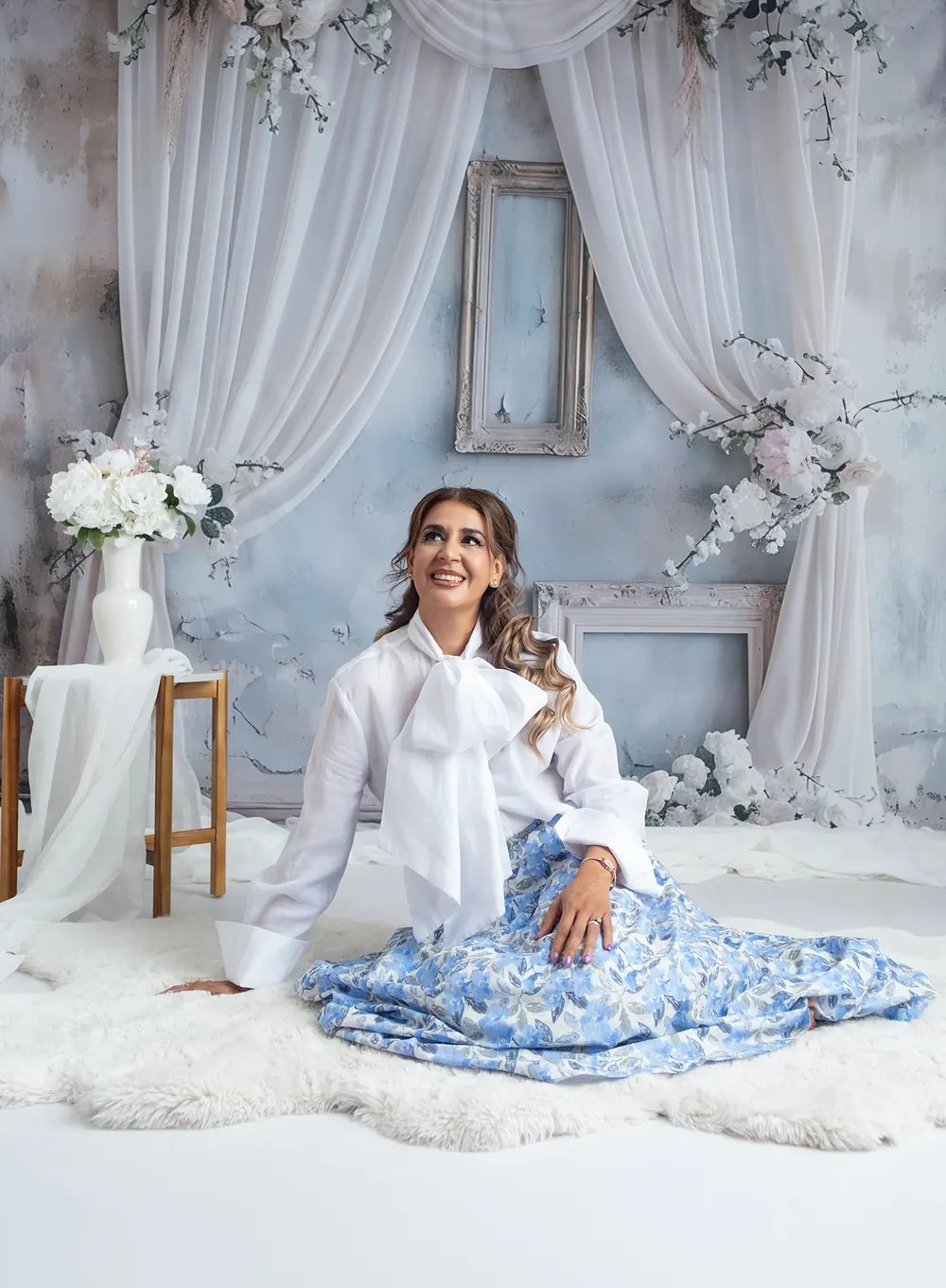 Alma Sández hoy, sentada en el piso con blusa blanca y falda azul, mirando hacia arriba con una sonrisa