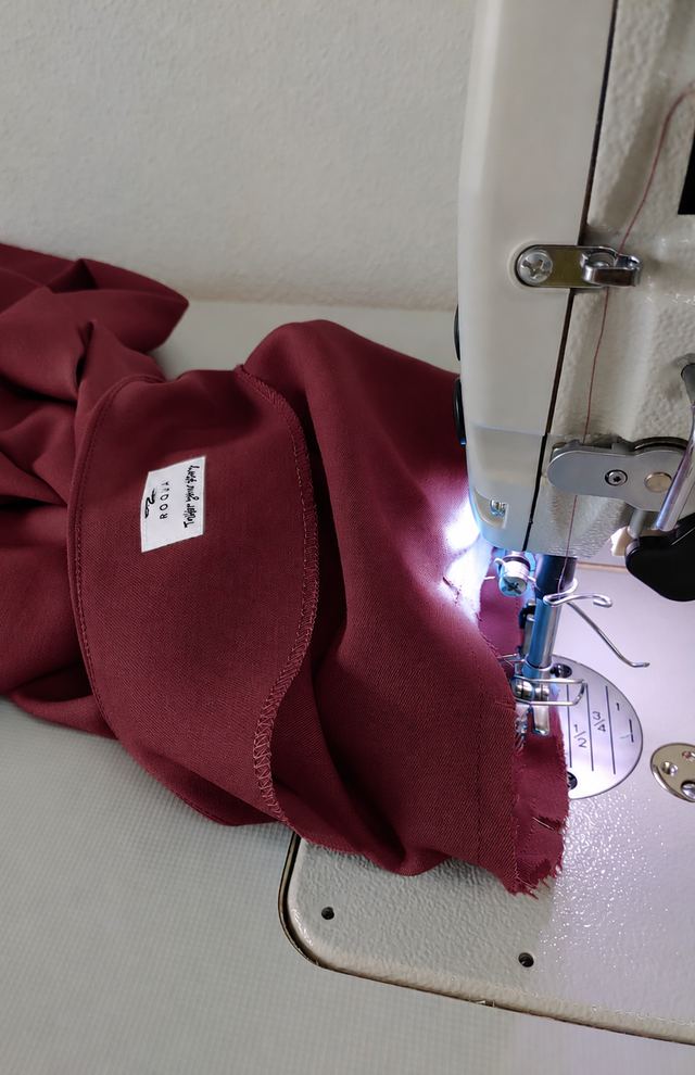 Bordeaux fabric with a ROQUA label being sewn at the machine