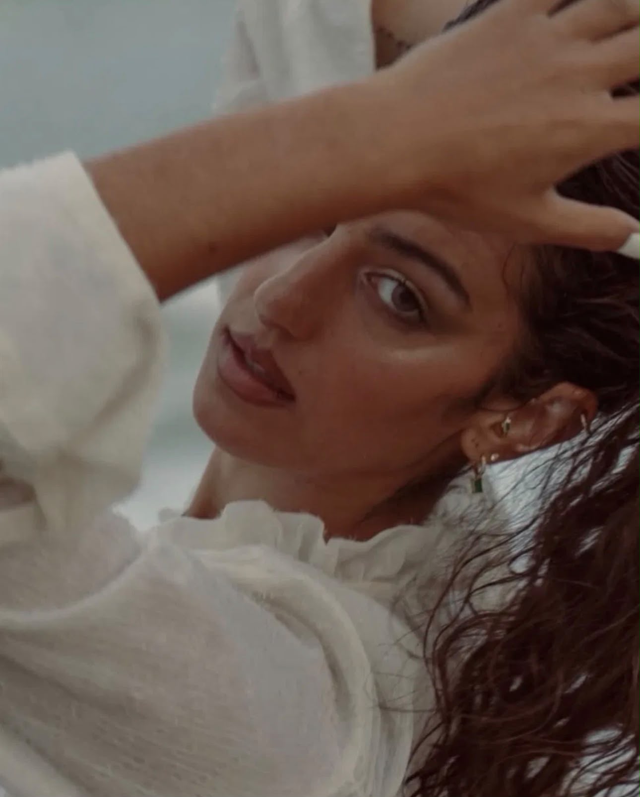 By the sea, hand raised to wet hair