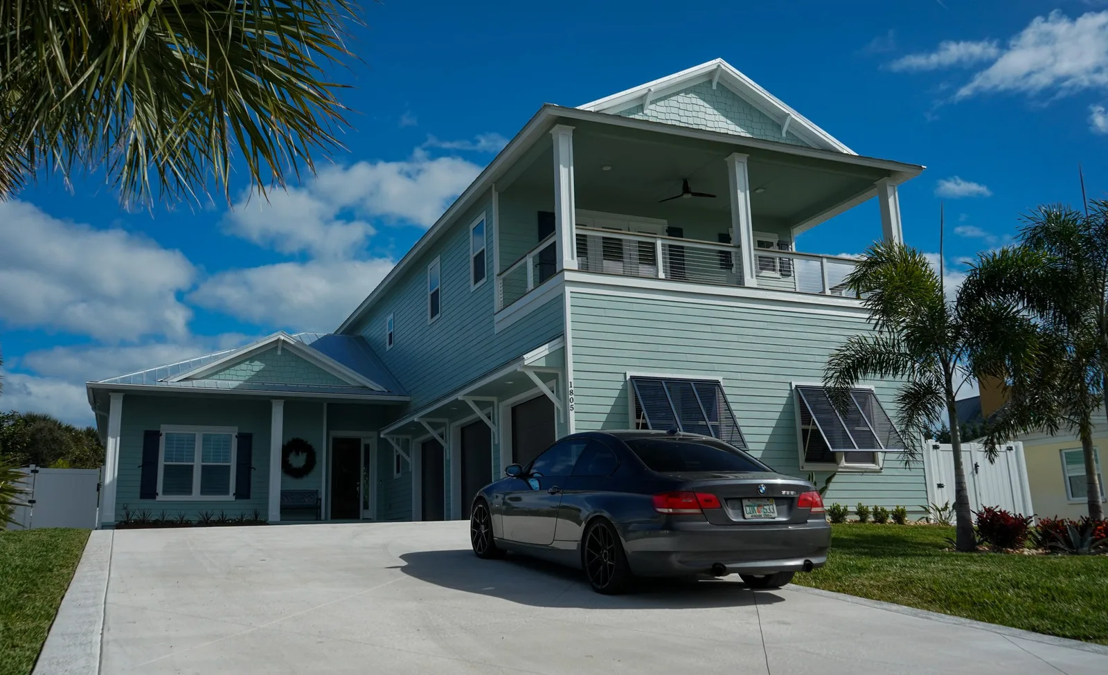 Two-story sage green coastal home with fresh exterior paint and white railings