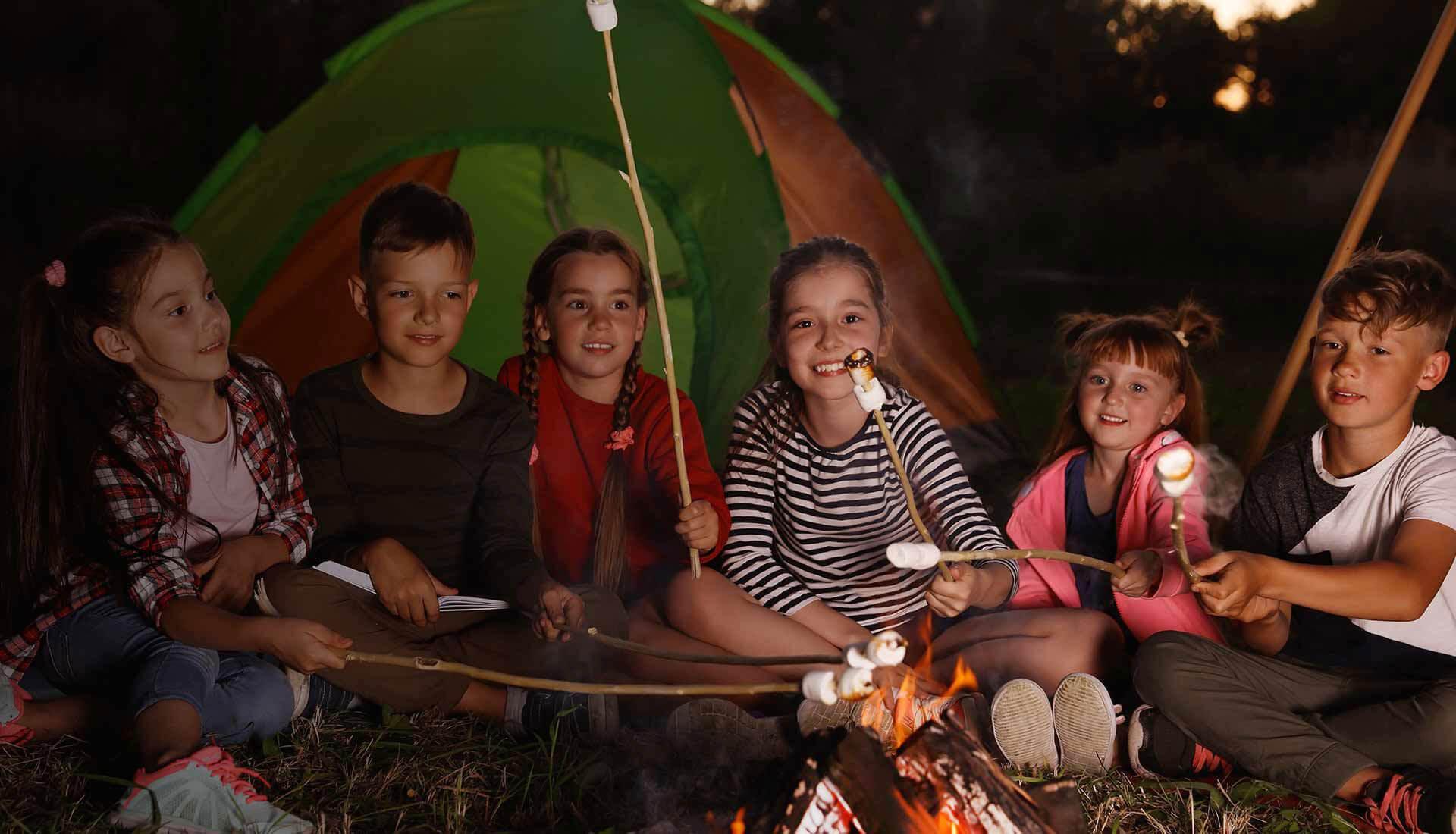 Kinderen rond het vuur met marshmallows voor de tent