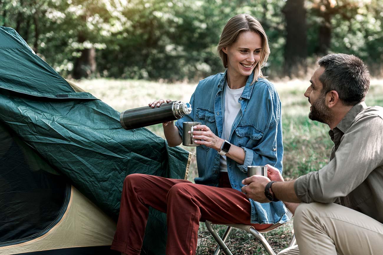 Twee gasten zitten voor de tent met een drinkfles, in de schaduw