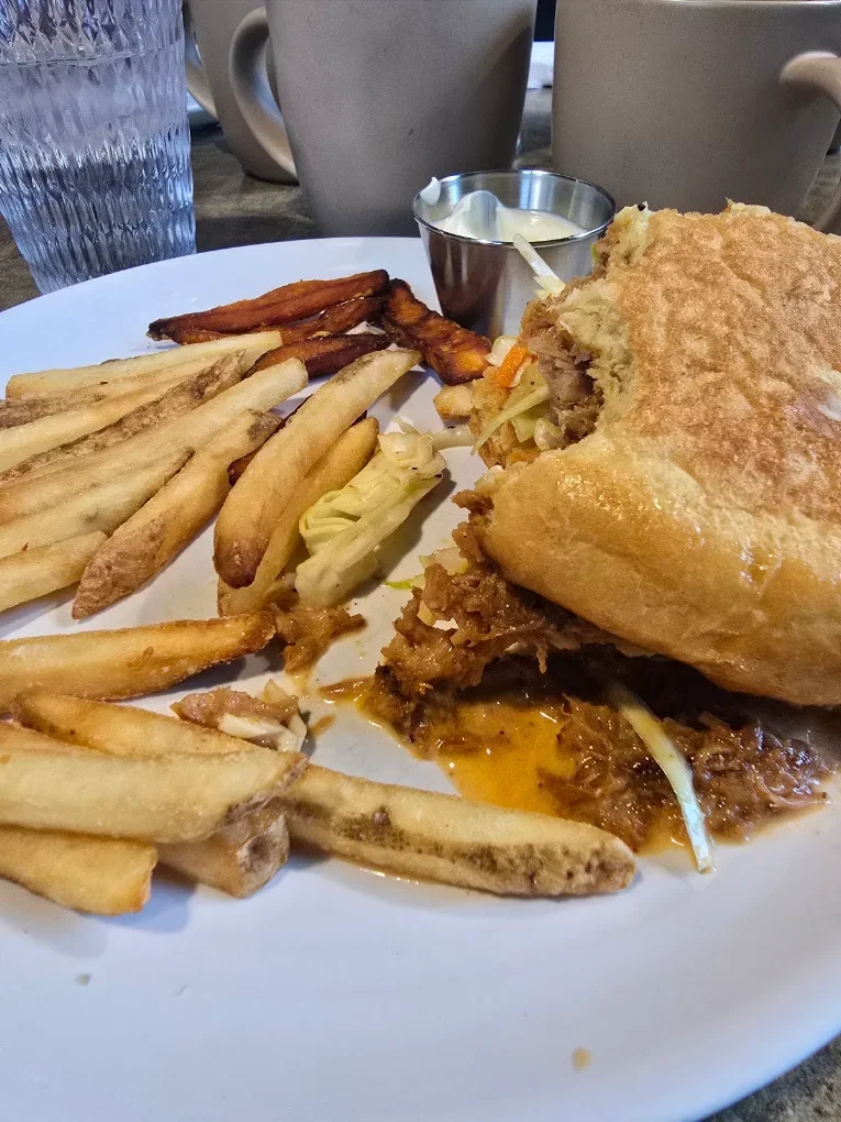 BBQ pulled pork sandwich with fries and sweet potato fries on a plate from The Harvest Table diner