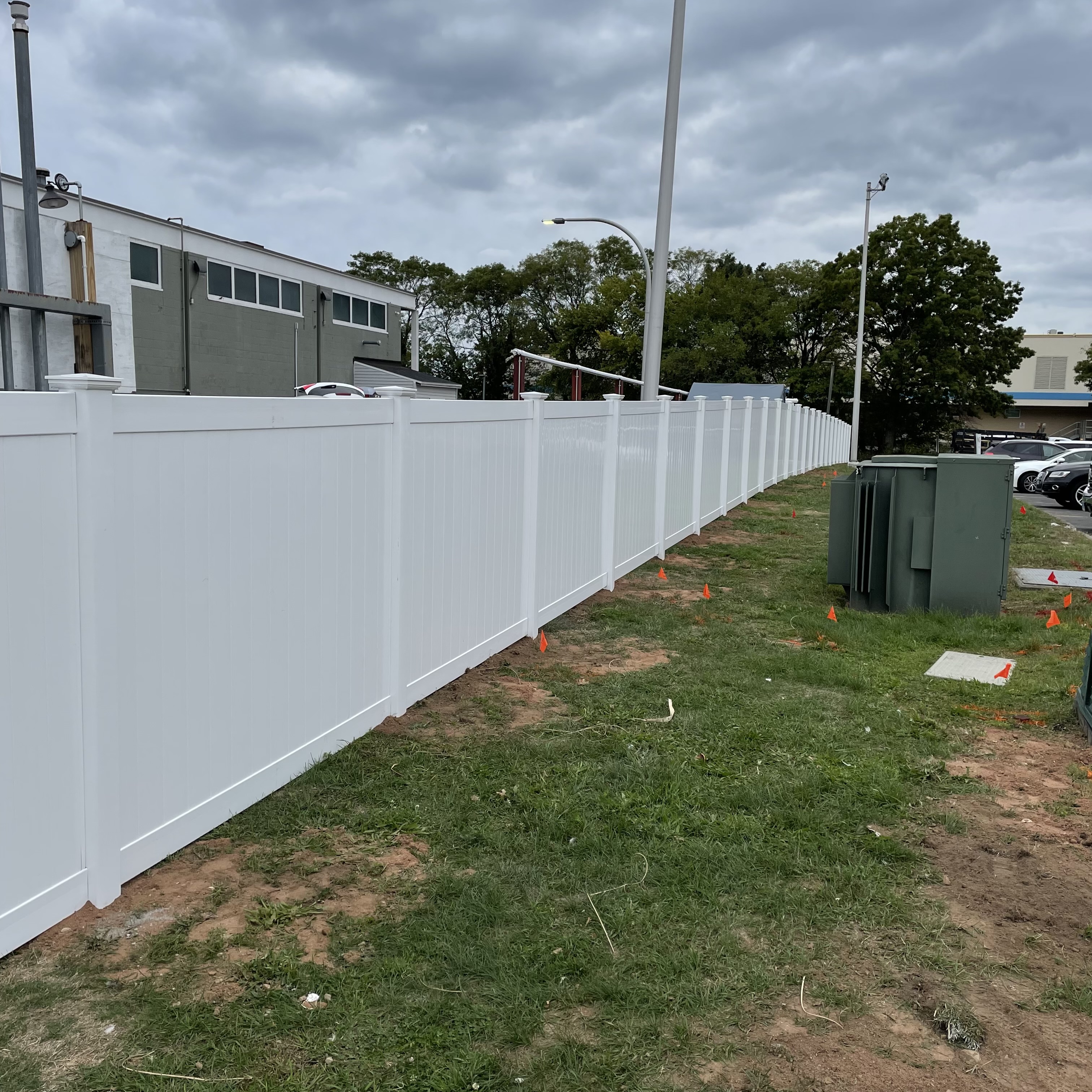 White fence with a grassy area and trees and buildings behind