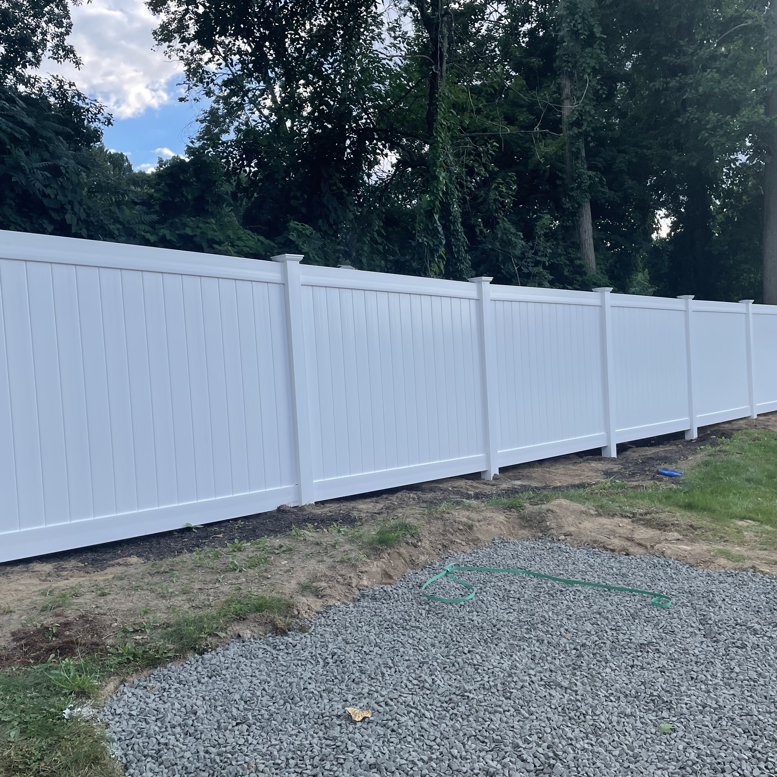 White fence with trees in the background and gravel in the foreground