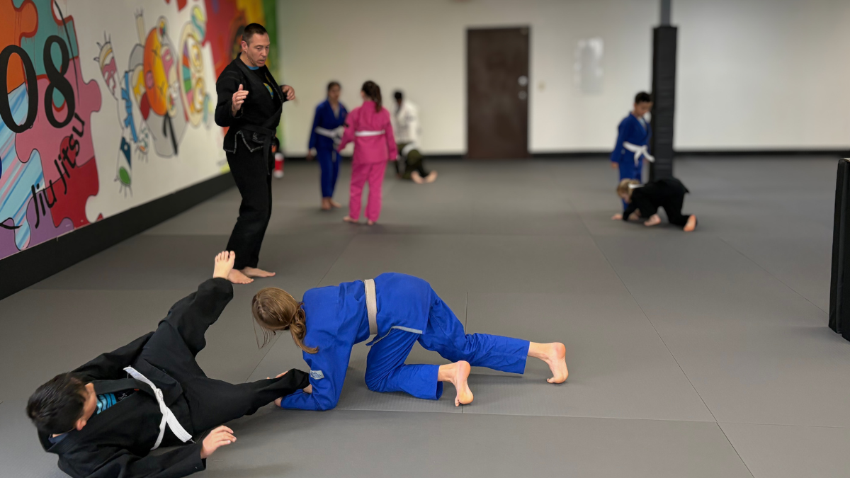 Two Champions students practice a jiu jitsu technique while Coach Joshua observes during class at 608 Jiu Jitsu.