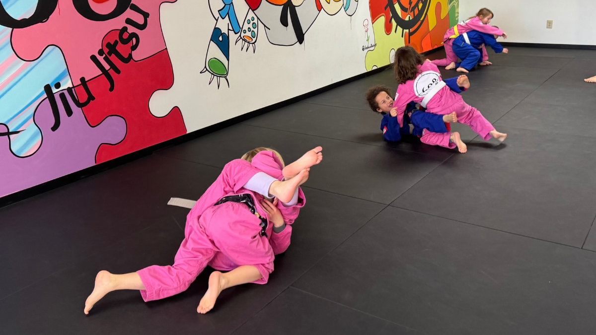 Three kids in pink jiu jitsu gis practice grappling together on the mat at 608 Jiu Jitsu.
